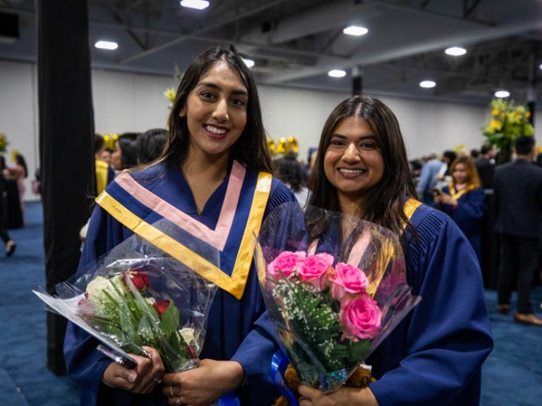 Two graduates smiling holding flowers