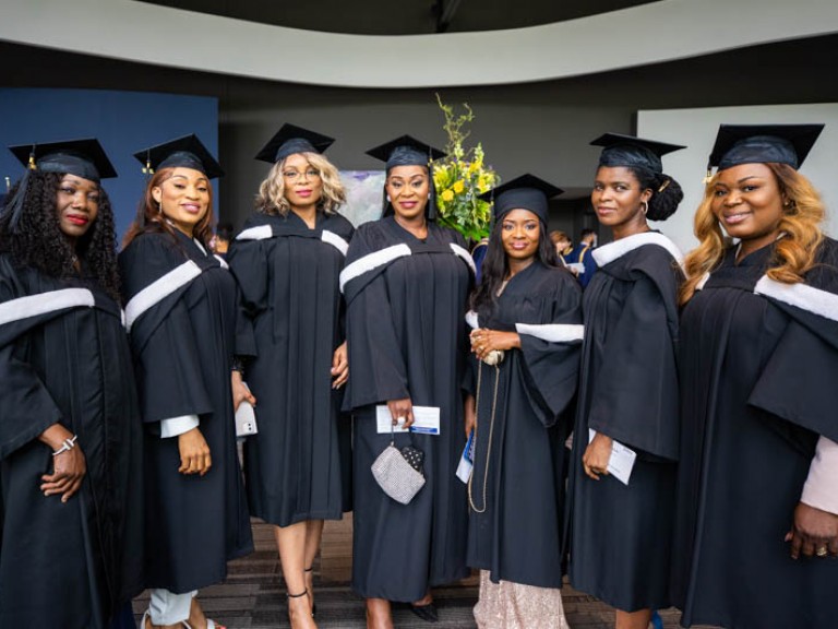 Seven graduates wearing black gowns and caps take photo together