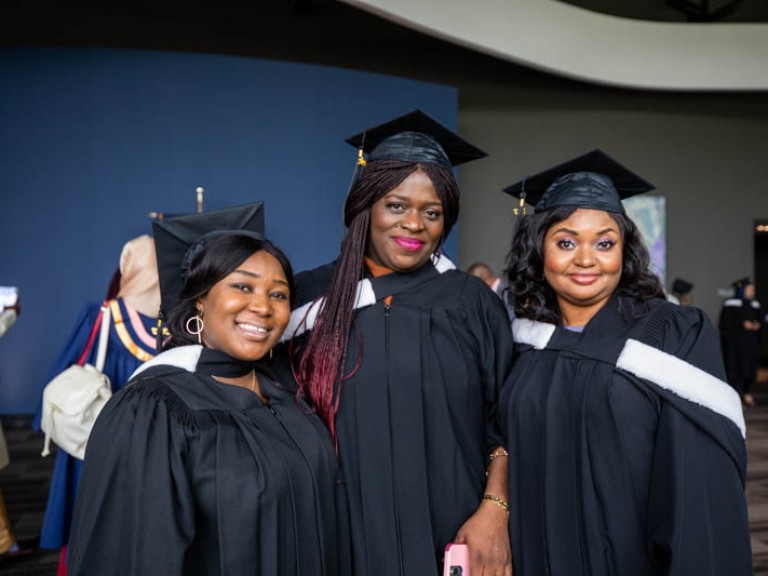 Three graduates wearing black gowns and caps pose together