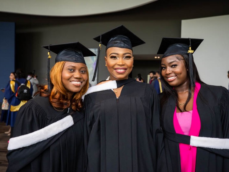 Three graduates wearing black gowns and caps smile for photo