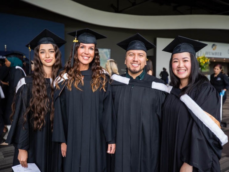 Four graduates in black gowns smile for photo