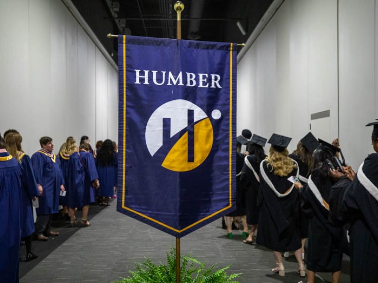 Humber flag in waiting area with lines of graduates on both sides