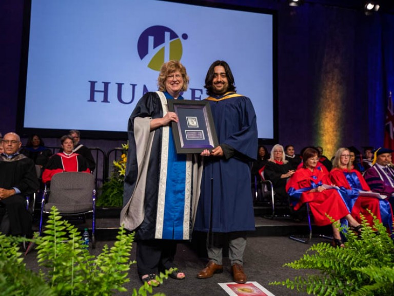 Graduate holds framed award beside Ann Marie