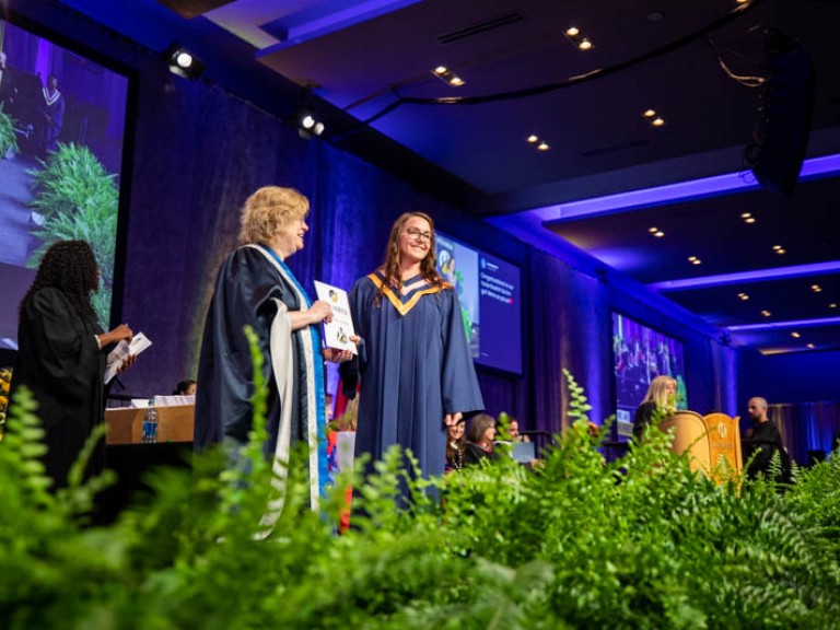 Graduate on stage poses for photo with Humber president