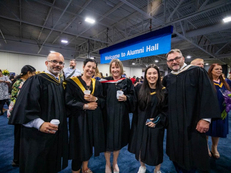 Five people wearing black robes smile for photo