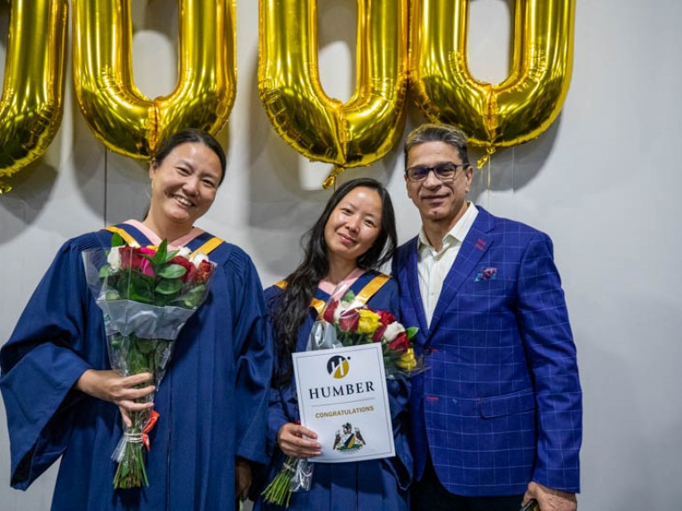 Two graduates and ceremony guest pose for photo