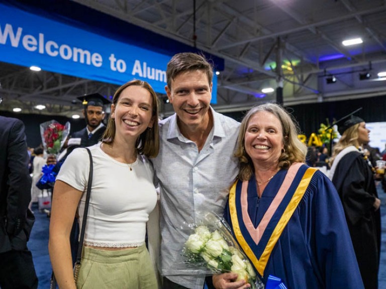 Graduate holding flowers takes photo with two family members