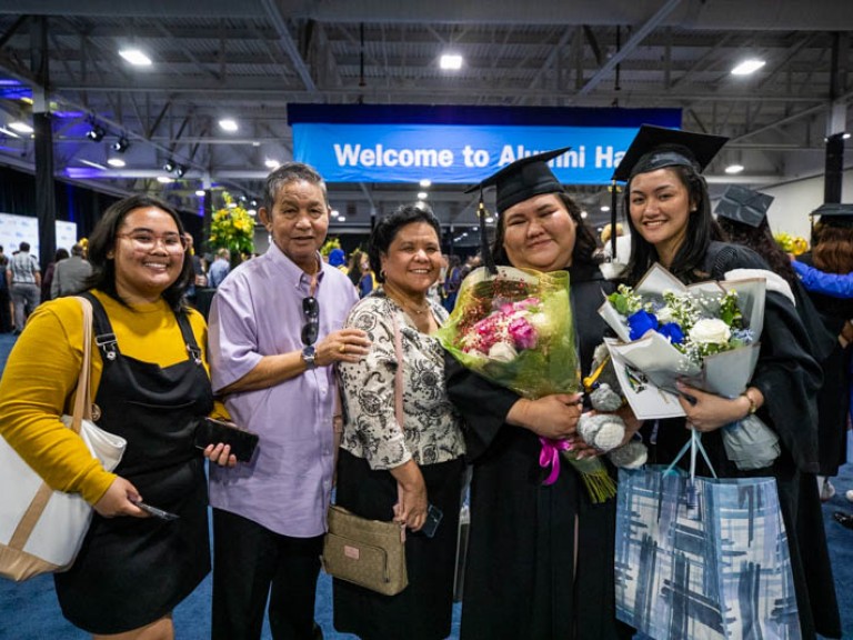 Two graduates holding flowers pose with three guests