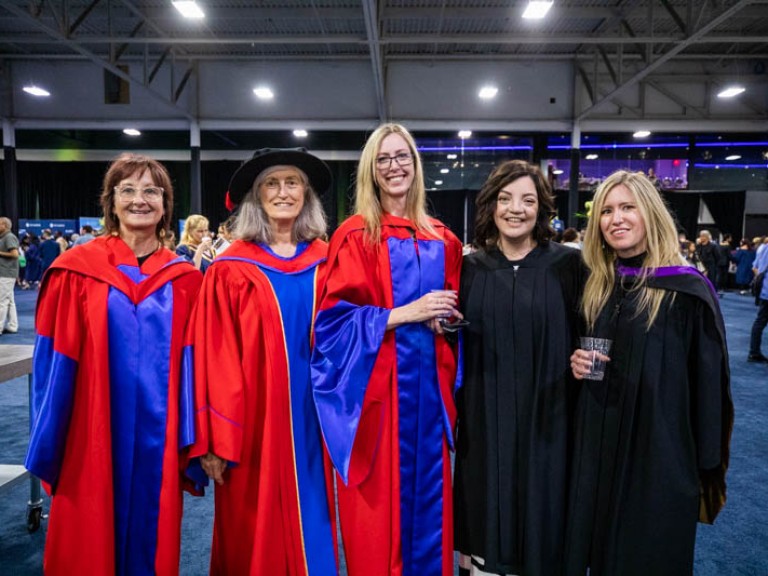 Five people in gowns pose for photo