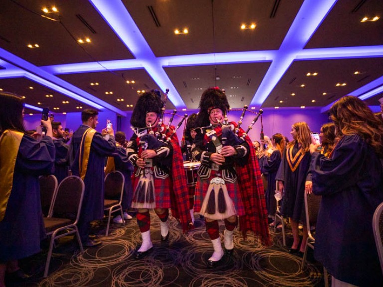 Two people in Scottish attire playing bagpipes walk down ceremony aisle