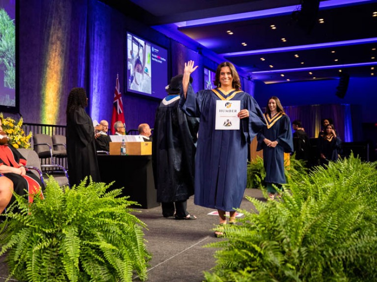 Graduate waves at photographer as they cross stage