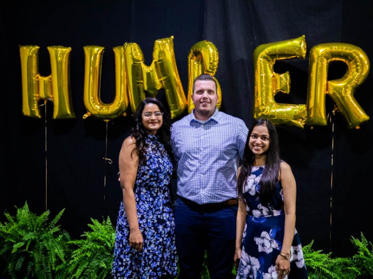 Three people take photo in front of gold HUMBER balloons
