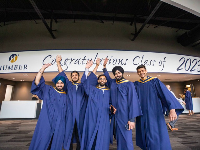 Five graduates raise arms in celebration underneath Congratulations Class of 2023 sign
