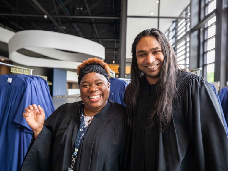 Two people wearing black robes smile for camera
