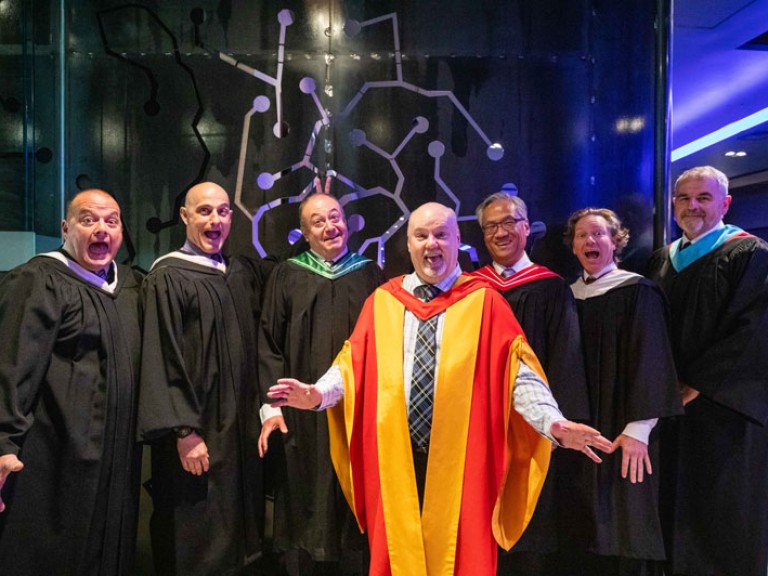 Seven faculty members in robes with excited expressions