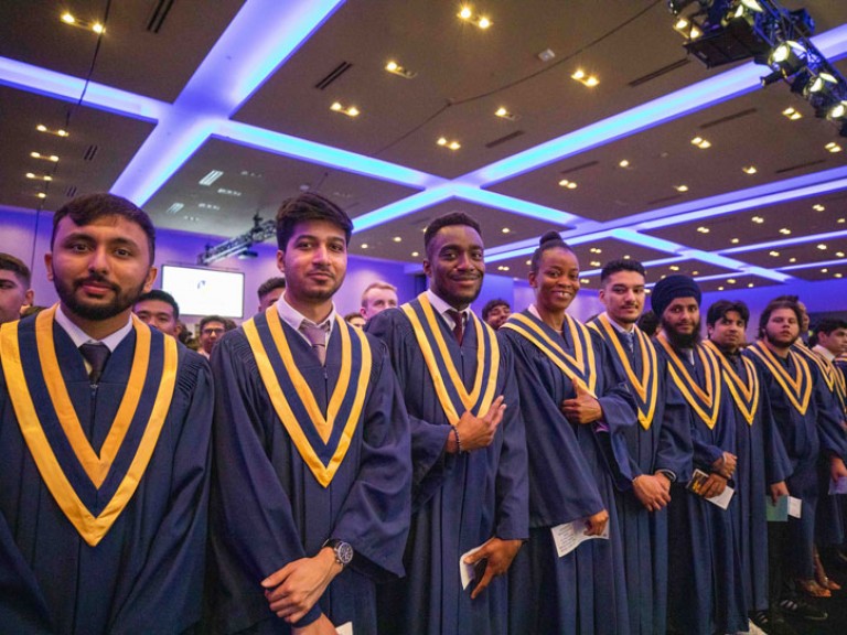 Row of standing graduates look at camera