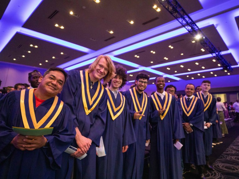 Row of standing graduates smile at camera