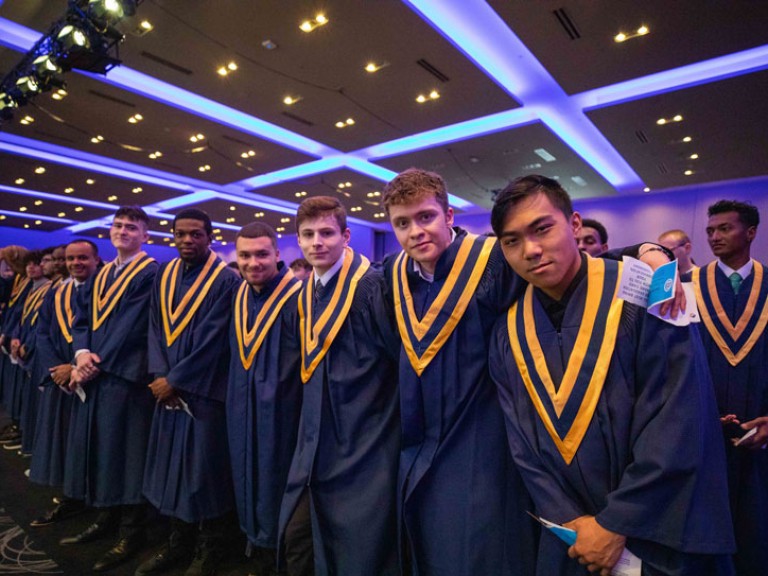 Row of graduates in ceremony hall pose for camera