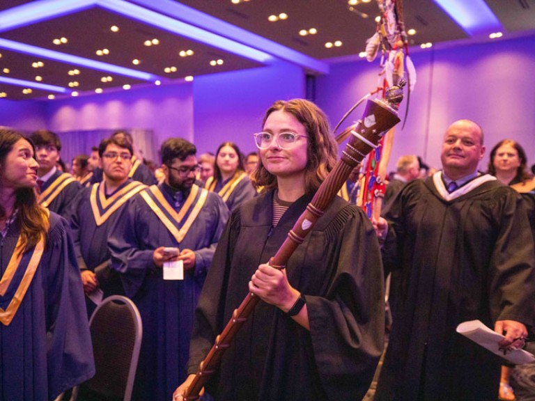 Person carrying ceremonial staff walks down aisle