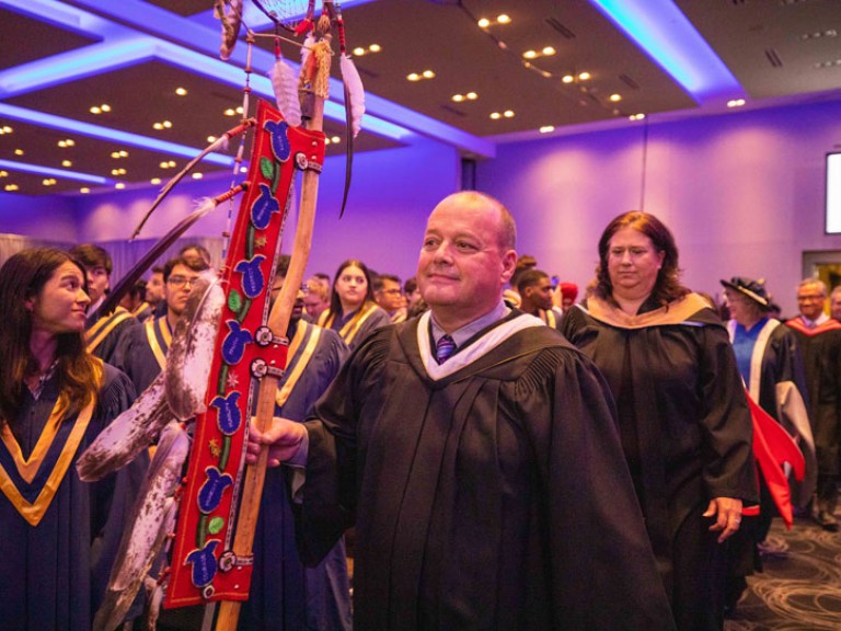 Person carrying Indigenous banner walks down ceremony aisle
