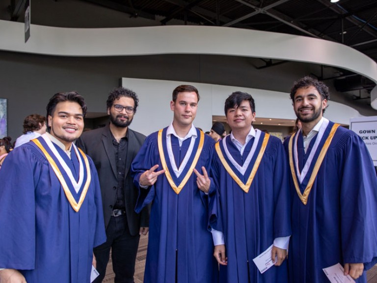 Four male graduates posing with ceremony guest