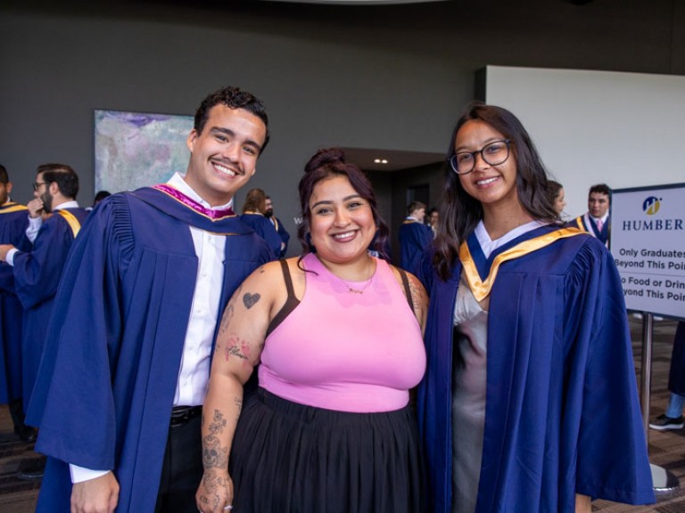 Two graduates and ceremony guest smile for photo