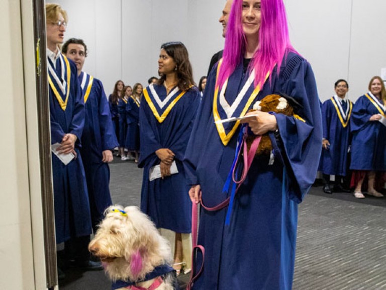Graduate with pink hair holds their dog's leash