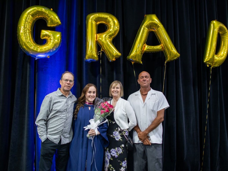 Graduate poses with three family members underneath GRAD balloons