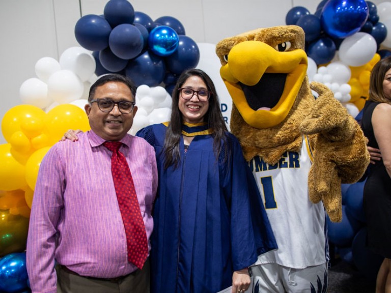 Graduate poses with family member and Humber mascot in front of balloons