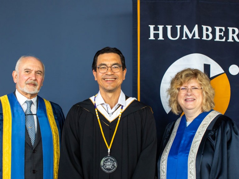 Three people pose in front of Humber flag