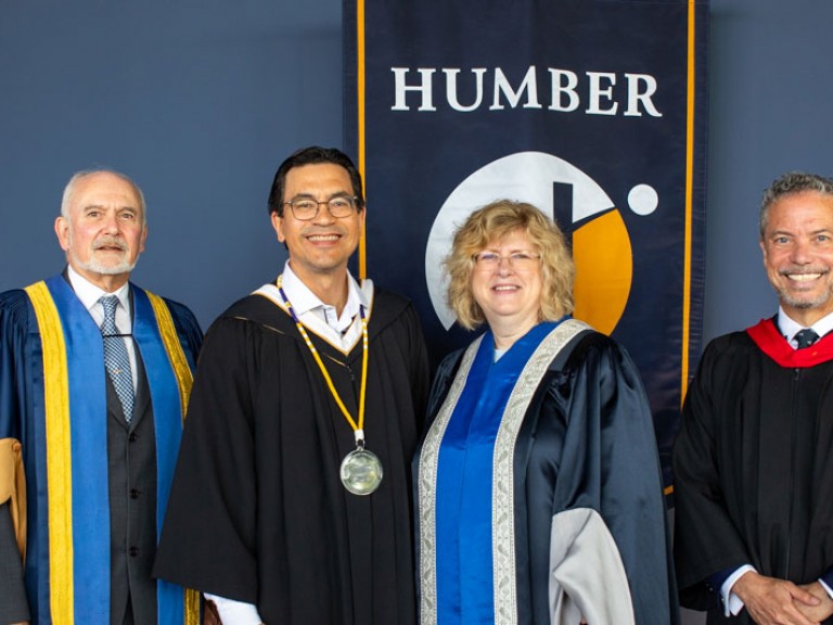 Four people pose in front of Humber flag