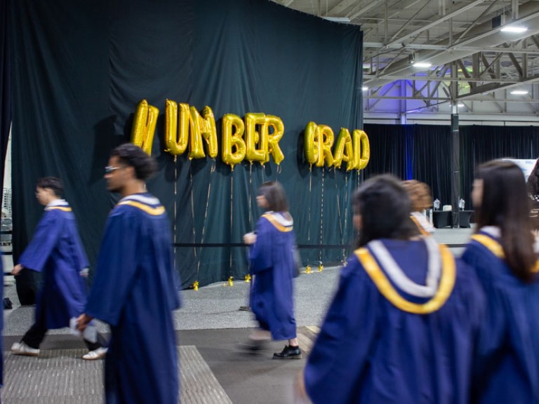 Humber graduates walking past gold Humber Grad balloons