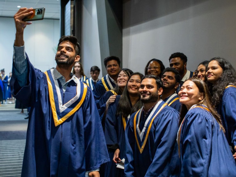 Graduate taking a selfie with a group of graduates behind him