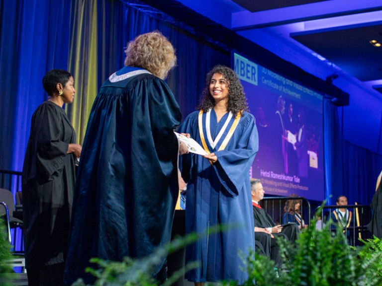 Graduate on stage smiling as they receive certificate