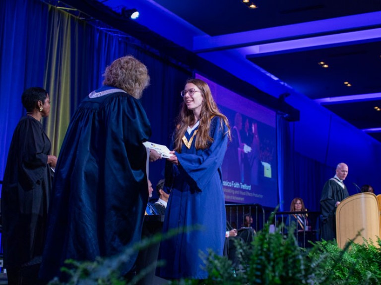 Graduate on stage smiling as they receive certificate from Humber president