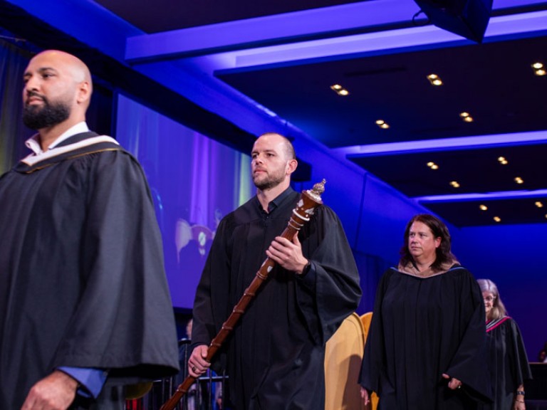 Humber faculty member carrying ceremonial staff proceeds in line