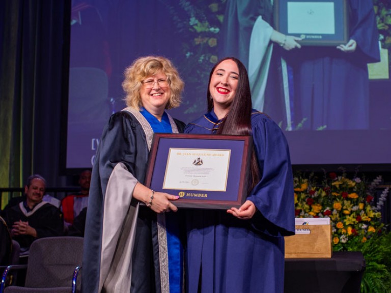 Graduate accepts framed award from Humber president