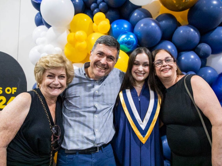 Graduate takes photo with three family members in front of balloons