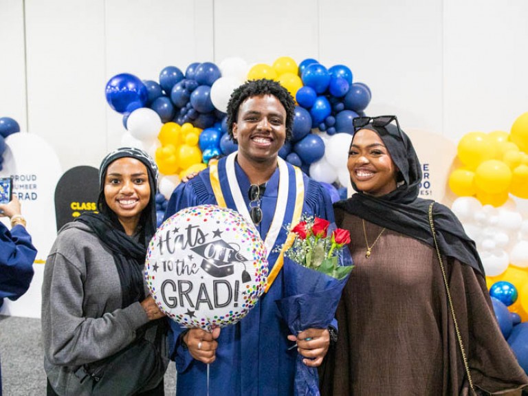Graduate holding balloon and roses takes photo with two others