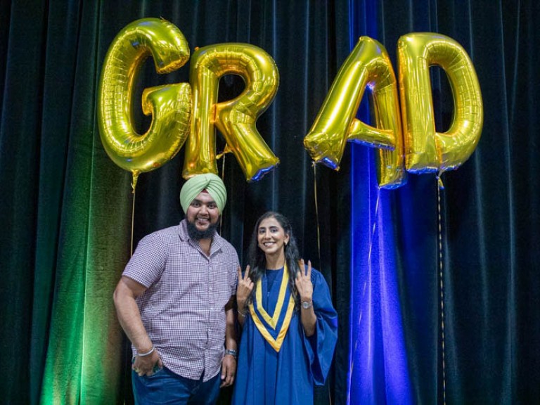 Graduate takes photo under GRAD balloons with ceremony guest