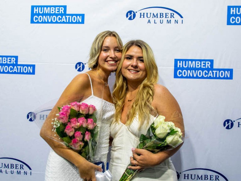 Two people holding bouquets in front of Humber Convocation photo wall