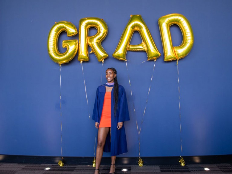 Graduate poses for photo beneath GRAD balloons