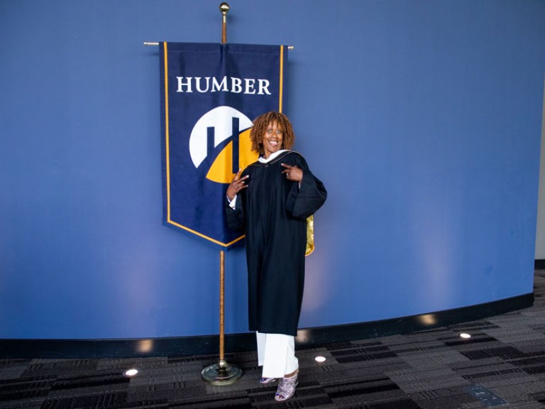 Honorary degree recipient Jacqueline Edwards poses for photo in front of Humber flag