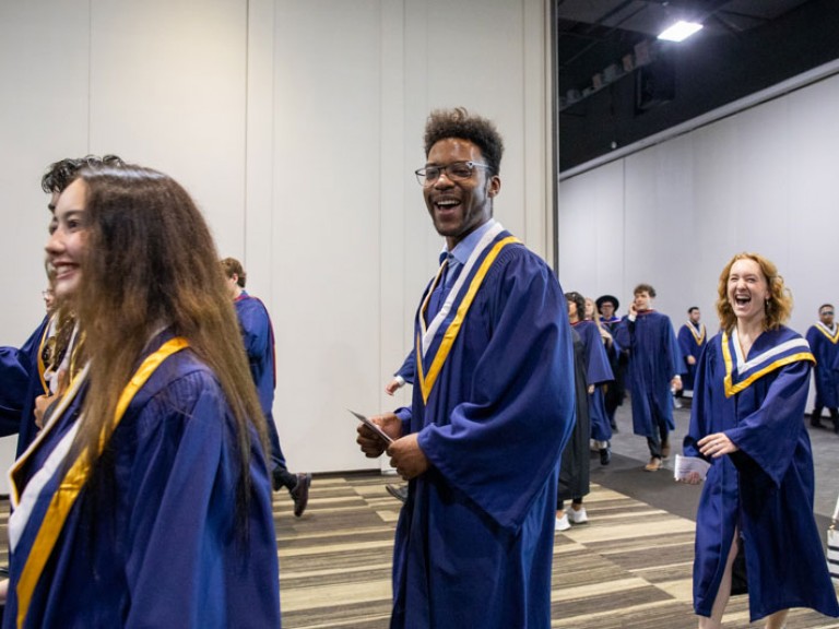 Graduate smiles at camera as they walk into ceremony