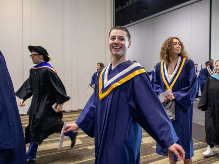 Graduate smiles at camera as they walk into ceremony
