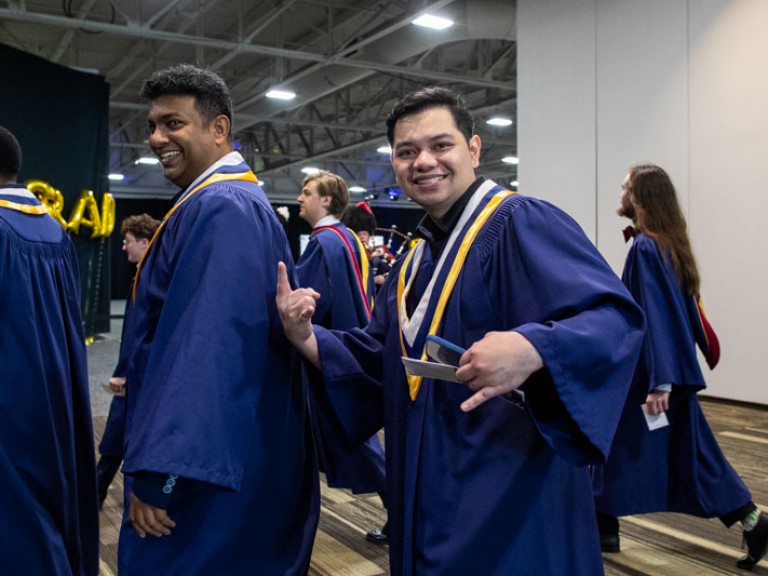 Two graduates smile as they walk by camera