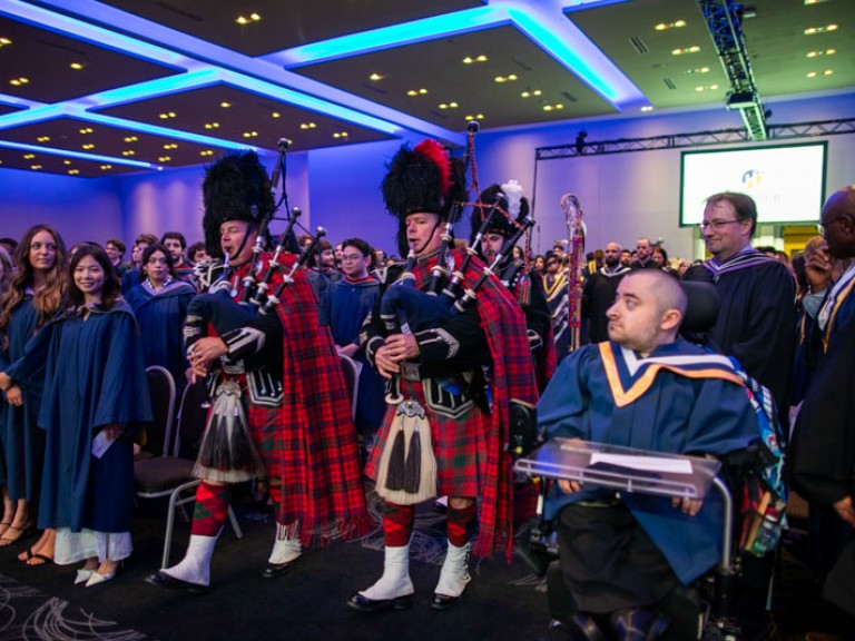 Bagpipe players in formal kilt attire enter the ceremony room