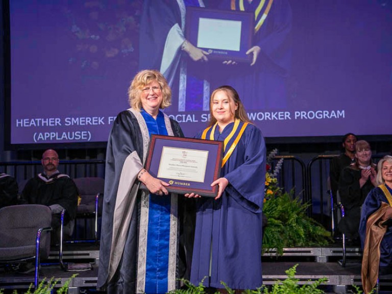 Graduate holds up framed award with Humber president
