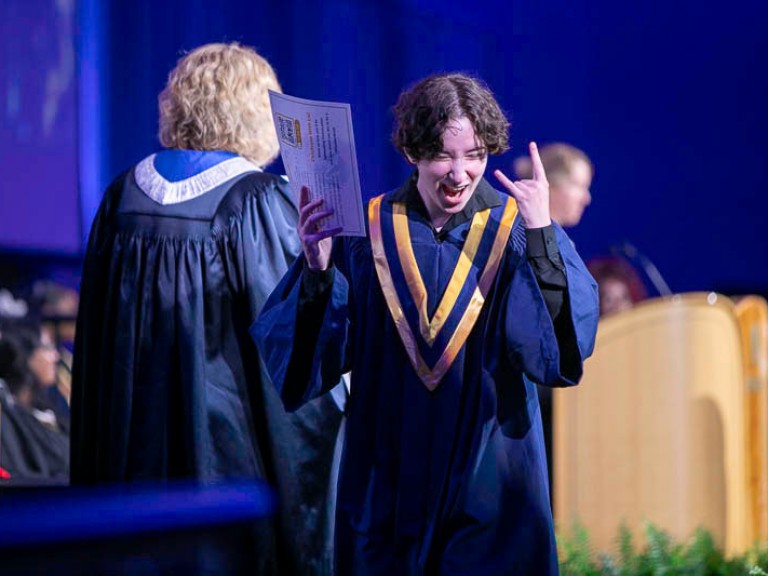 Graduate makes hand sign as they leave stage