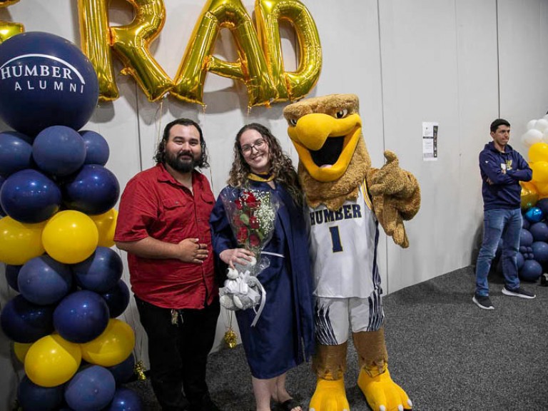 Graduate takes photo with ceremony guest and Humber mascot